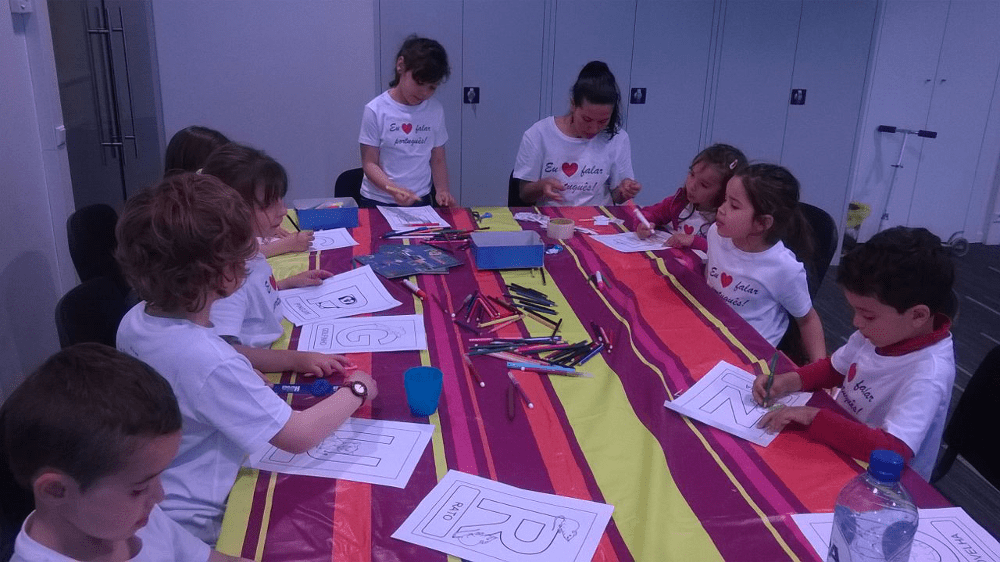 Un groupe d'enfants assis autour d'une table. Ils colorient des morceaux de papier avec de grosses lettres