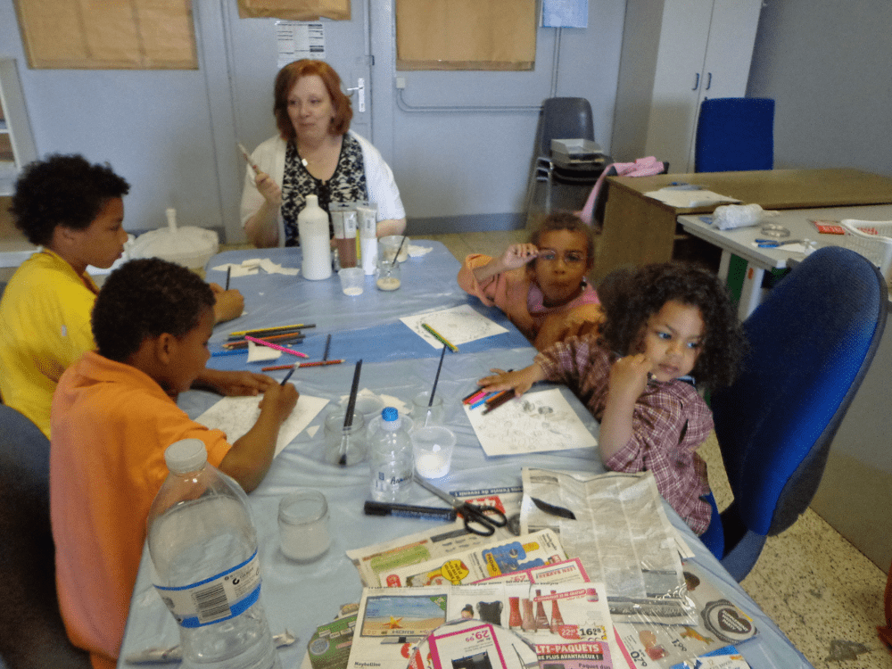 Une femme et quatre jeunes enfants assis à une table en trein de faire des dessins et d'autres œuvres d'art