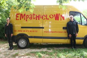 Deux personnes vêtues de noir, avec des nez de clown, devant la camionnette Empathiclown