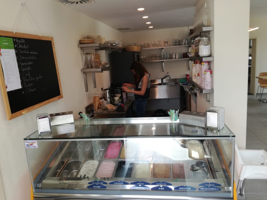femme travaillant dans une petite cuisine professionnelle. vers le spectateur se trouve un comptoir avec de la crème glacée