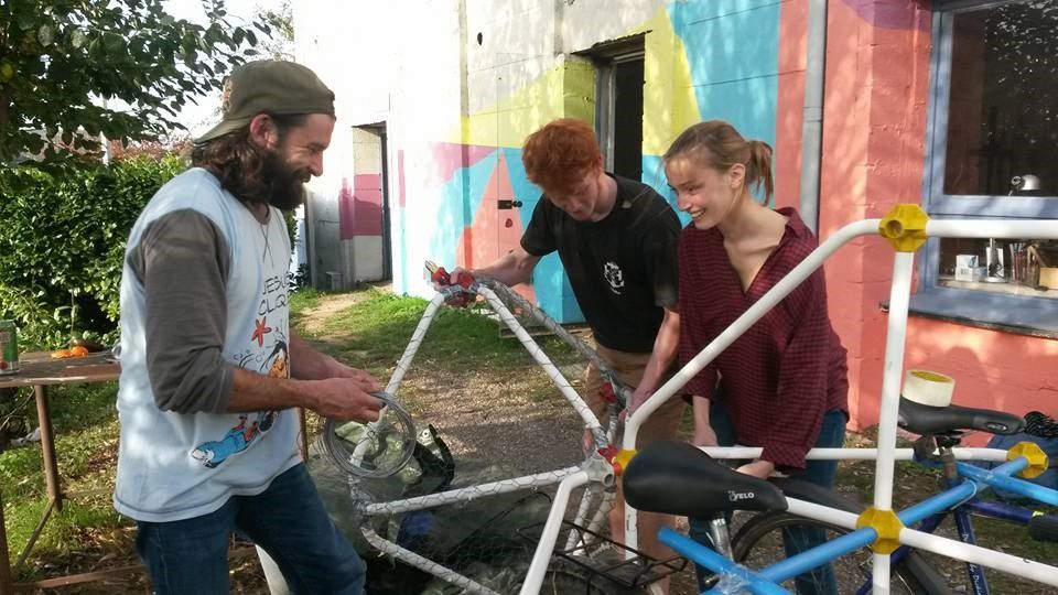 Trois jeunes souriants travaillant avec différents objets métalliques et un vélo