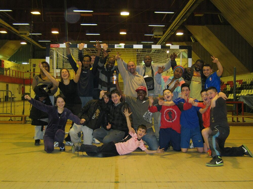 Un groupe d'adultes et d'enfants riant posant pour la caméra dans une salle de sport couverte. Beaucoup d'entre eux lèvent les mains et les bras