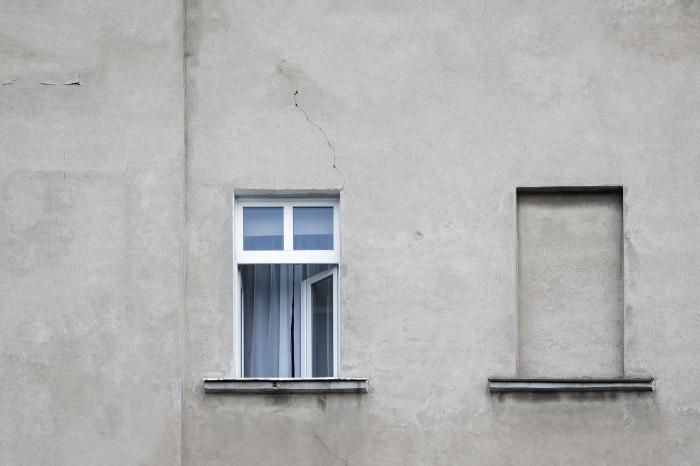 Photo d’illustration d’un large mur gris avec une fenêtre ouverte et une fenêtre murée.