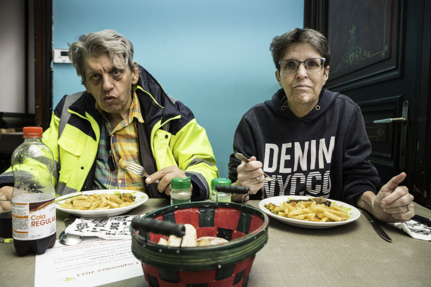 Un homme et une femme à table en devant des assiettes de frites et de viande.