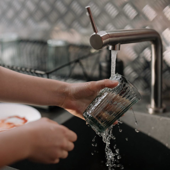 une paire de mains en train de laver un verre sous un robinet