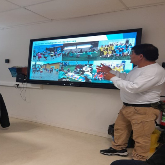 Une personne à coté d'un écran parle en faisant des gestes soulignants