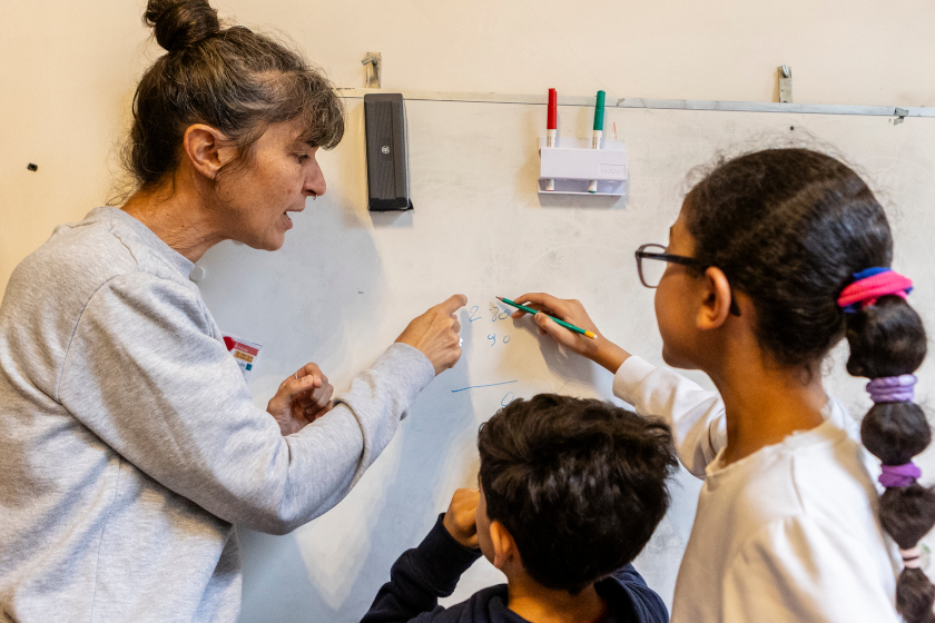 Deux enfants et un adulte devant un tableau.