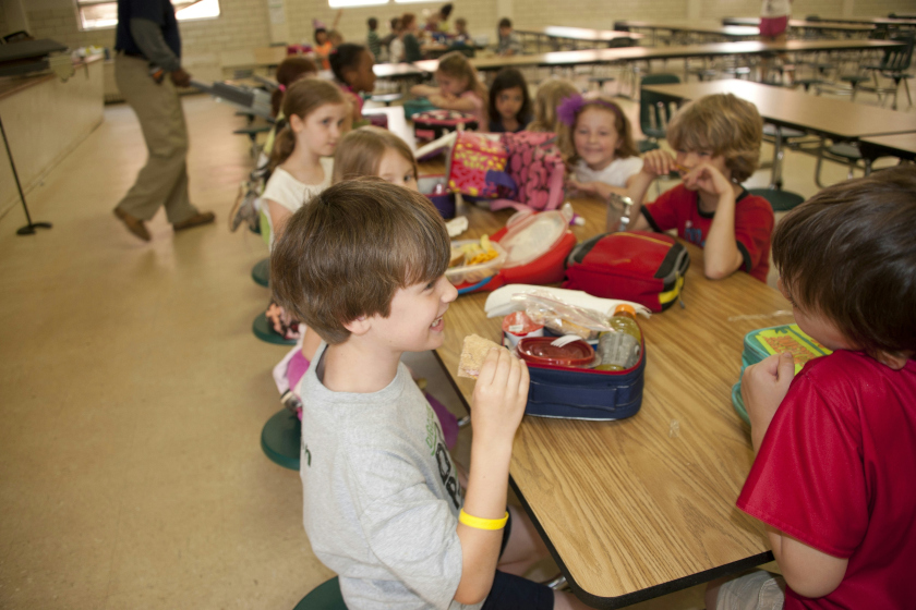 Des enfants avec leur boites à tartines autour d'une table de cantine en train de manger